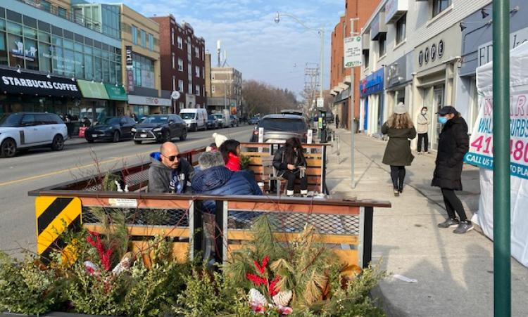 People sitting on benches enjoying the parklet on Spadina Rd. 